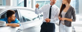 Car Salesman Giving a Key From the New Car to the Young Owners